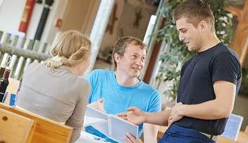 A server helps patrons at a restaurant. File photo courtesy of © Can Stock Photo / kadmy.