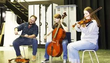 Cam Bowman demonstrating bowing to Hannah Hewitt (Cello) and Jalyssa Martin (violin). Photo provided by Banding Together.