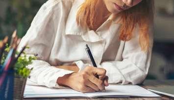 A woman writing into a book. File photo from Pra-chid/iStock / Getty Images Plus.