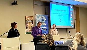 BWDSB honoured at BRAVO Awards.  Left to right: BWDSB Intermediate Senior Technology Coach Hillary Weppler, Communications Officer Jamie Pettit (at podium), and Director of Education Lori Wilder presenting at board meeting on November 19, 2024. Photo from BWDSB