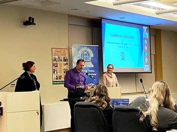 BWDSB honoured at BRAVO Awards.  Left to right: BWDSB Intermediate Senior Technology Coach Hillary Weppler, Communications Officer Jamie Pettit (at podium), and Director of Education Lori Wilder presenting at board meeting on November 19, 2024. Photo from BWDSB