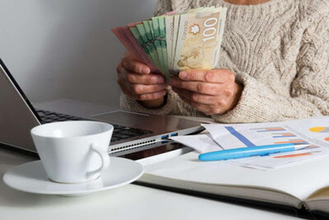 A person holding Canadian money sitting at a desk with bills and a laptop. Picture submitted by CNW Group and Unifor