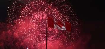 Fireworks light up the sky behind a Canadian flag. (Photo by Maureen Revait, Blackburn News)