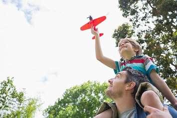 A little boy sits on his father's shoulders flying a toy plane. File photo courtesy of © Can Stock Photo / 4774344sean