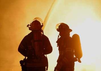 Two firefighters are silhouetted against a raging fire.  © Can Stock Photo / southpaw3