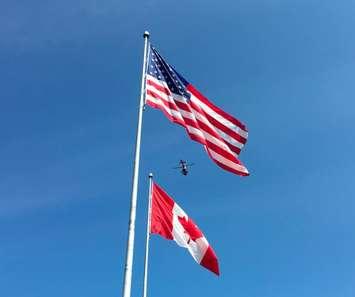 A Canadian Coast Guard helicopter flies high above the US and Canadian flags. (Photo by CCGS)