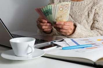 A person holding Canadian money sitting at a desk with bills and a laptop. Picture submitted by CNW Group and Unifor